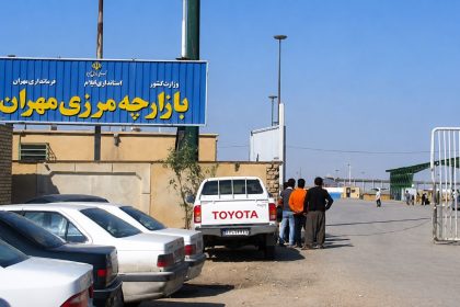 Entrance to the Zurbatia–Mehran border crossing with Iran, showing the border market gate, parked vehicles, and travelers.