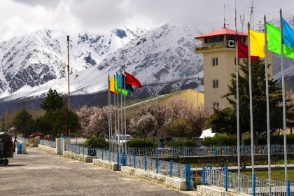 Skardu Airport air traffic control tower surrounded by colorful flags and the snow-covered Karakoram mountains in Gilgit-Baltistan, Pakistan.