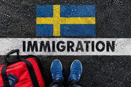 Swedish flag painted on a road above the word immigration, with a red travel bag and blue shoes at the border line.
