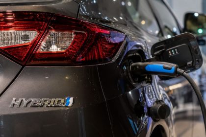 Close-up of a hybrid vehicle plugged into a charging station, showing the charging port and hybrid badge.