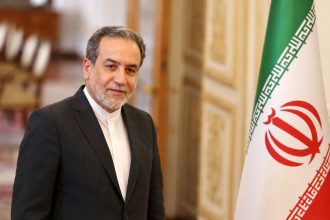 Iranian Foreign Minister Abbas Araghchi standing beside the Iranian flag.