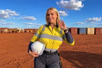 AI-generated image of Bindi Raye in mining workwear holding a white hard hat at a worksite.