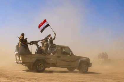 Houthi fighters riding in a pickup truck with a Yemeni flag