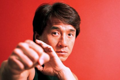Jackie Chan posing with his fists raised against a red background.