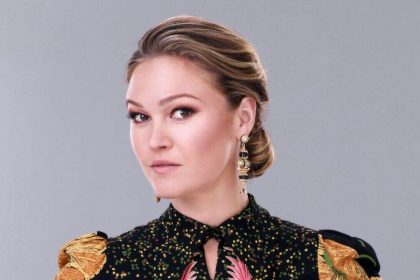 Julia Stiles posing for a portrait in a black patterned outfit.