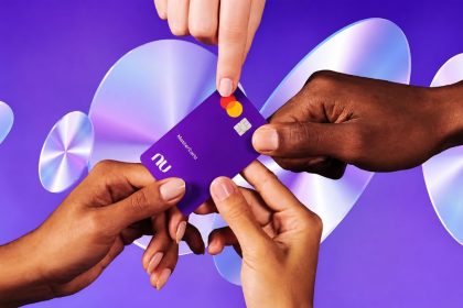 Hands exchanging a purple Nubank payment card against a purple background.