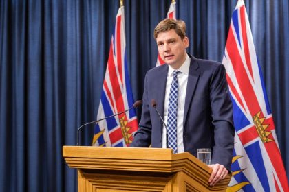 B.C. Premier David Eby speaking at a podium with British Columbia flags