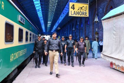 Pakistan Railway Police officers walk through Lahore Railway Station beside a passenger train.