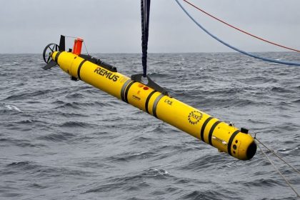 Yellow REMUS autonomous underwater vehicle suspended above the sea.