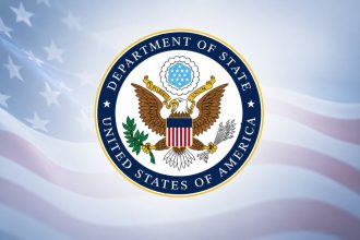 U.S. Department of State seal on an American flag background.