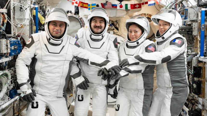 NASA’s SpaceX Crew-12 astronauts wearing white pressure suits and stacking their gloved hands inside a spacecraft module.