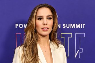 Christy Carlson Romano wearing a white blazer and posing in front of a purple event backdrop.