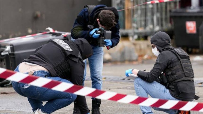 Forensic investigators in protective vests and gloves document evidence at a shooting scene in the Paris suburbs.
