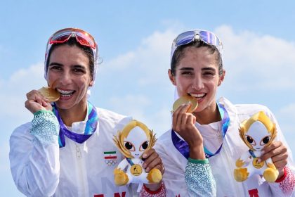 Iranian women athletes bite their gold medals while holding Asian Games mascots.