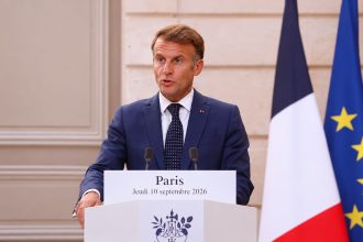 French President Emmanuel Macron speaking at a podium with French and European Union flags behind him.