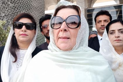 Noreen Niazi, sister of PTI founder Imran Khan, wearing a white headscarf and sunglasses outside a building.