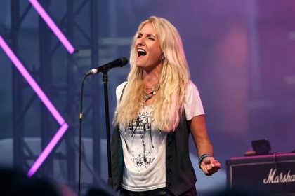 Sass Jordan singing into a microphone during a live performance.