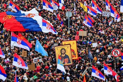 Crowd of protesters waving Serbian flags and holding banners and religious icons during a demonstration in Serbia in 2025.