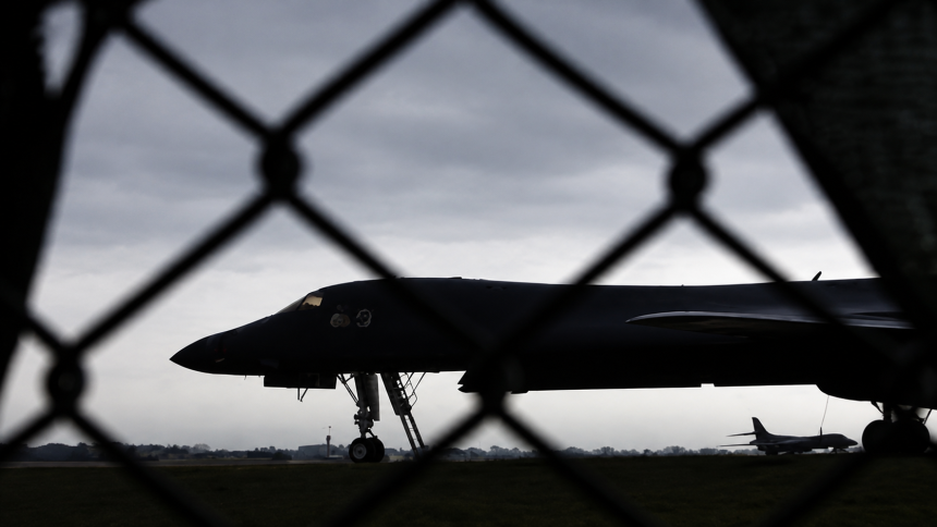 A U.S. military bomber sits on the runway behind a security fence at an air base.