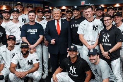 US President Donald Trump standing with New York Yankees players wearing team uniforms and caps in the clubhouse.